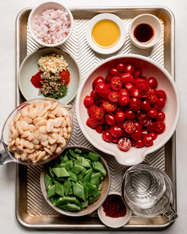 An overhead shot shows prepped ingredients for a saucy butter bean skillet recipe; all in small bowls or measuring cups on a baking sheet.