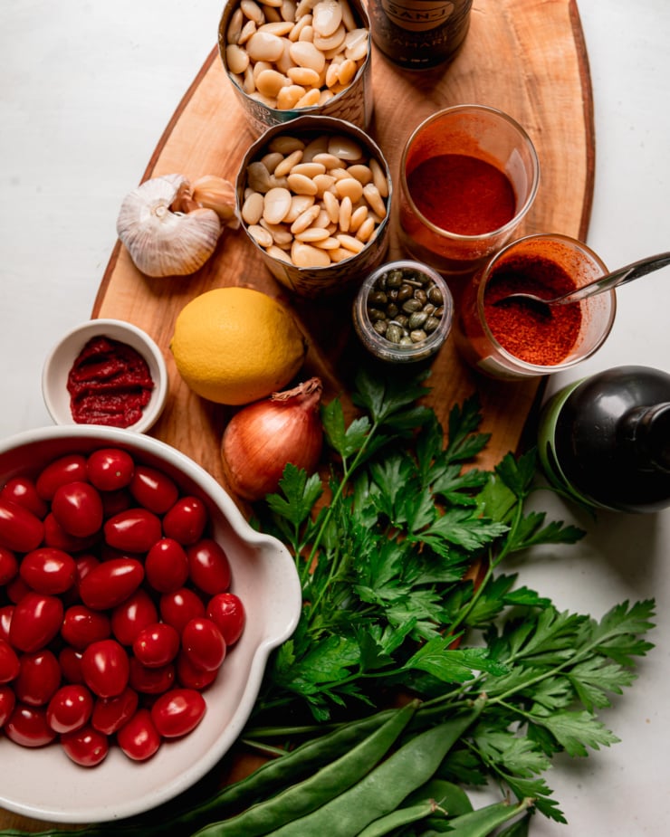 An overhead shot shows raw ingredients for a butter bean skillet recipe on a wooden cutting board.