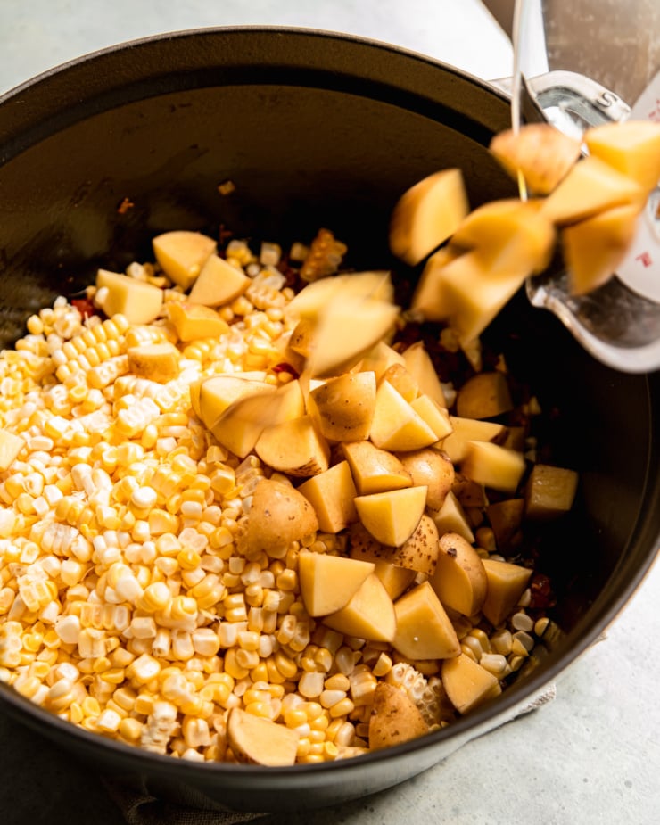 A 3/4 angle shot shows potatoes going into a large pot that is filled with fresh corn kernels.