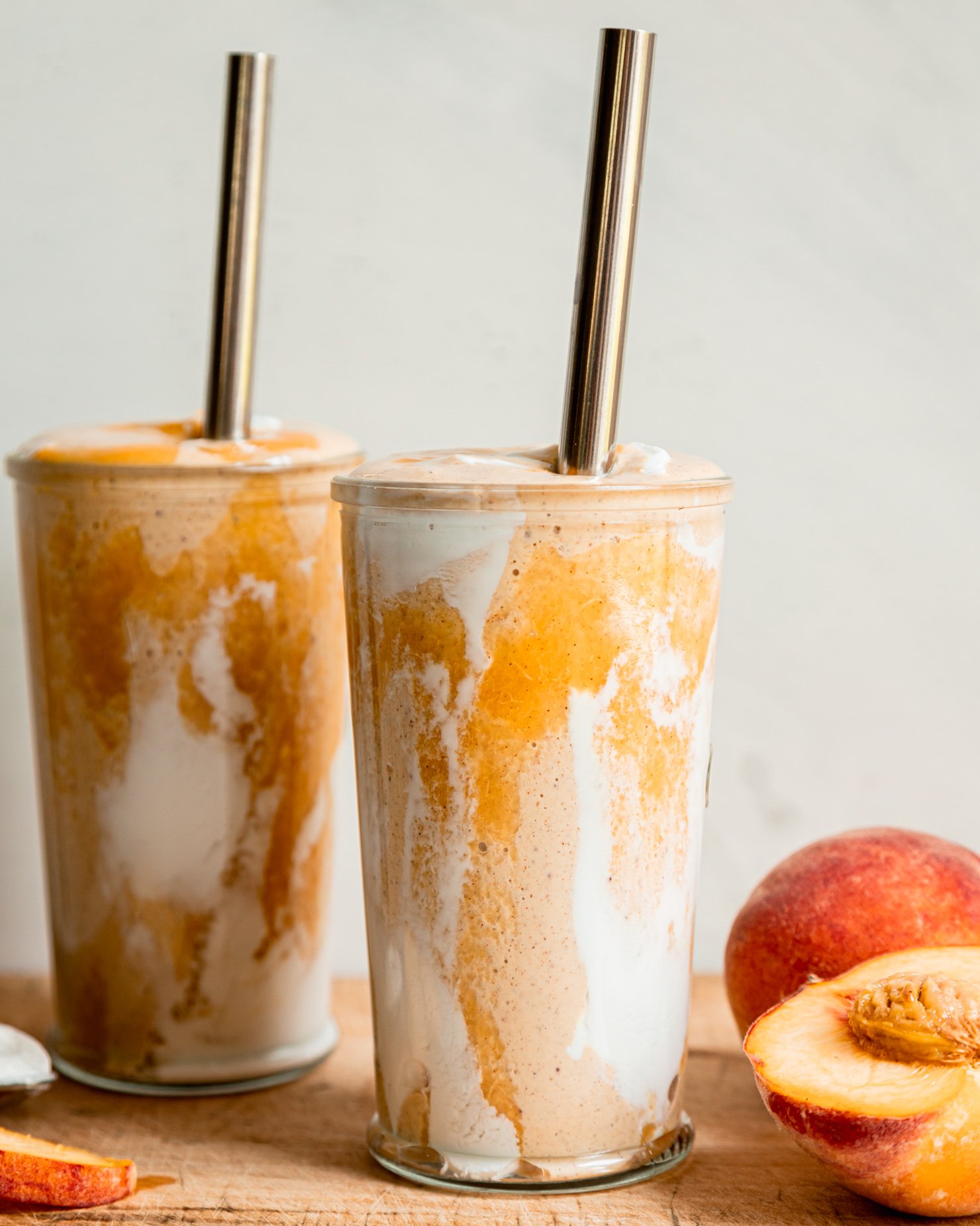 A head-on shot of a vegan peaches and cream protein smoothie in two glasses with metal straws. Peach purรฉe and vegan yogurt create a tie dye effect on the glass.