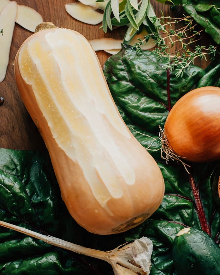 An overhead shot shows a peeled butternut squash on top of some chard greens.
