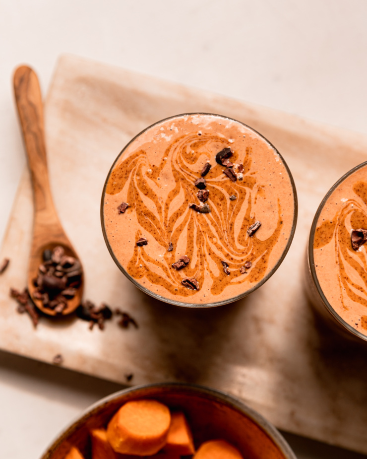 An overhead shot shows a glass of chocolate sweet potato smoothie with almond butter swirls and cacao nibs on top.