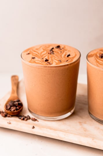 A head-on shot shows a glass of chocolate sweet potato smoothie with almond butter swirls and cacao nibs on top.