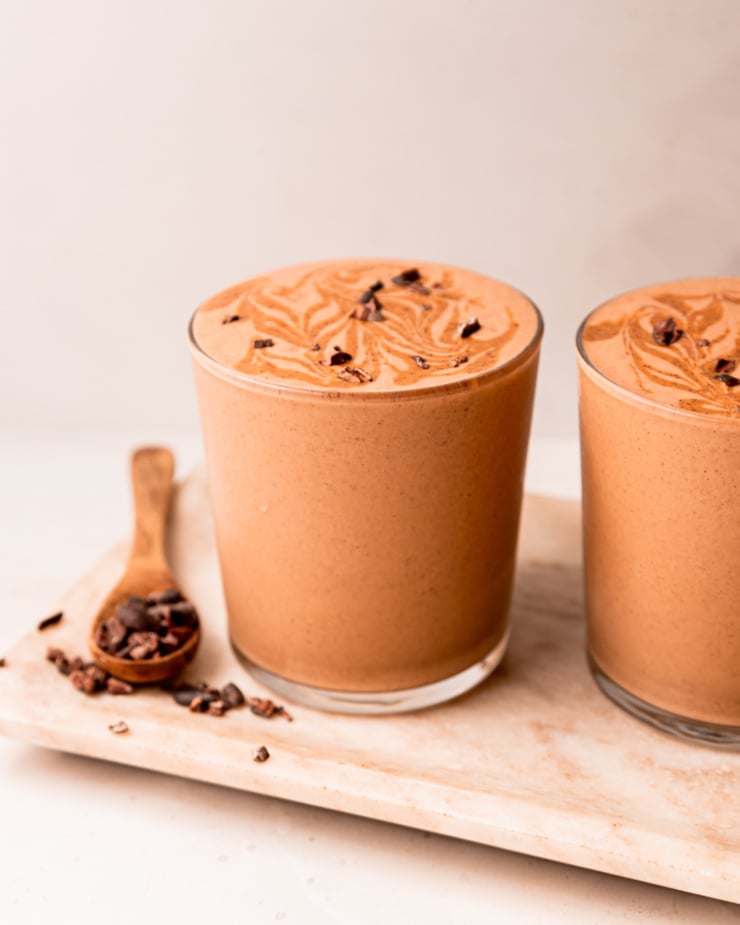A head-on shot shows a glass of chocolate sweet potato smoothie with almond butter swirls and cacao nibs on top.