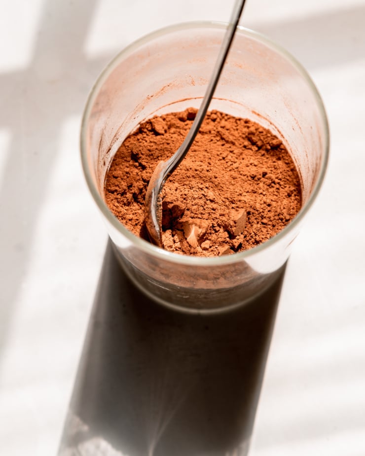 An overhead shot shows a glass canister of cocoa powder with a spoon inside.