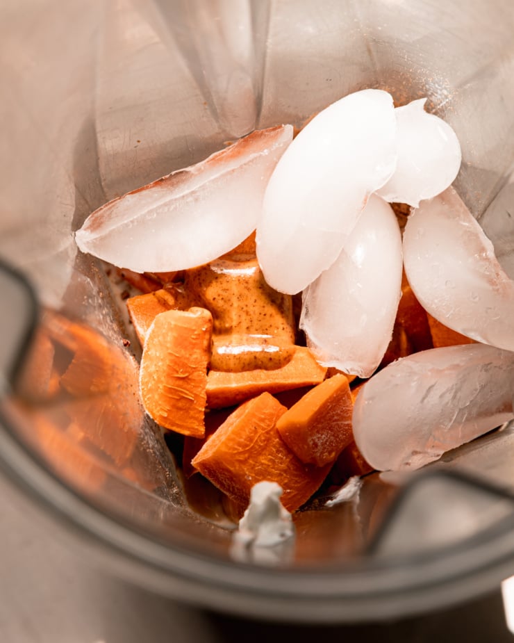 An overhead shot shows frozen cubes of sweet potato, ice, and almond butter in a blender pitcher.