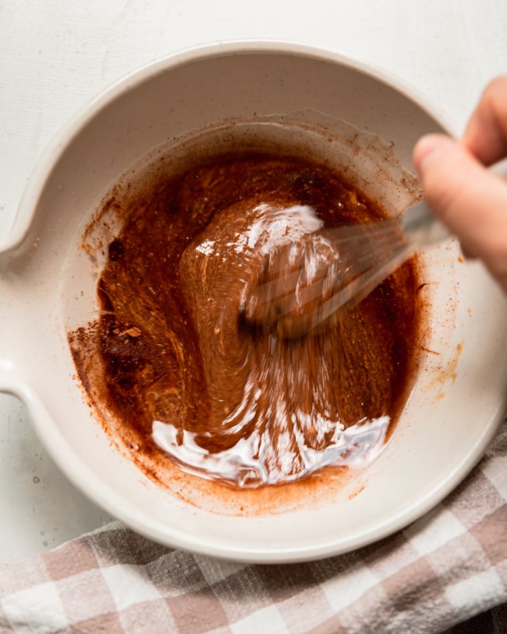 An overhead shot shows a hand using a whisk to being a mixture together in a bowl.