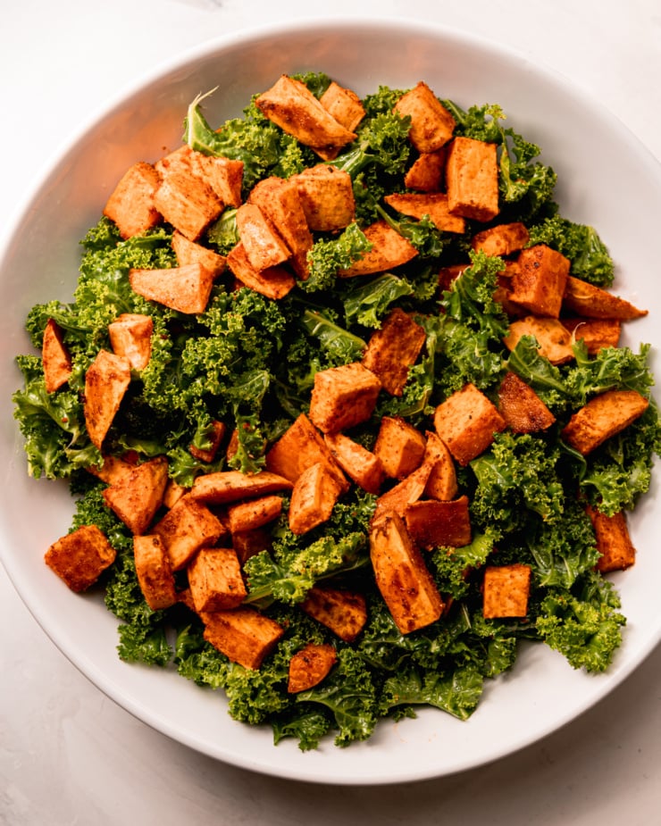 An overhead shot shows massaged chopped kale topped with spice-roasted sweet potatoes.