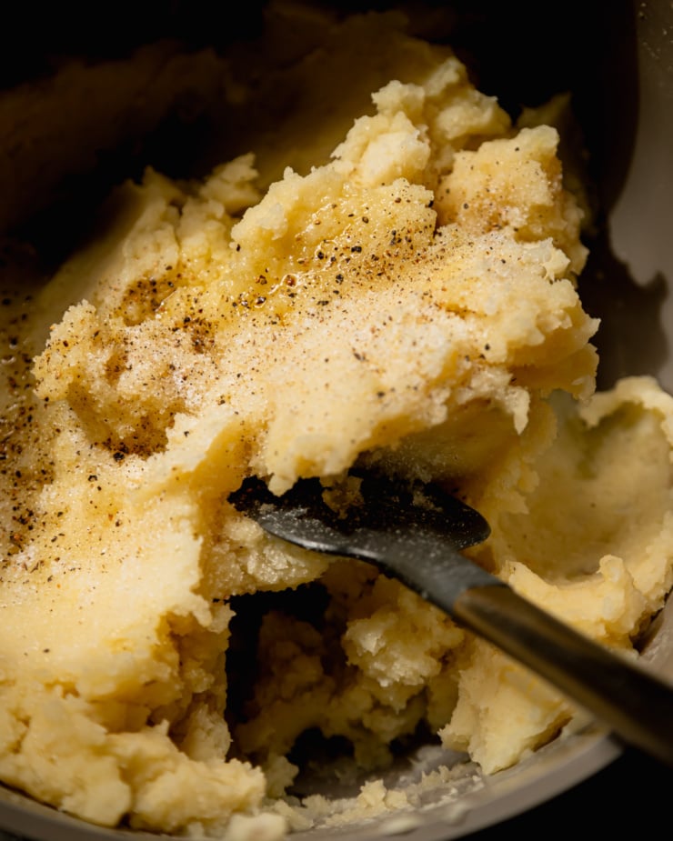 An up close, overhead shot shows olive oil mashed potatoes in a pot with salt and pepper on top.