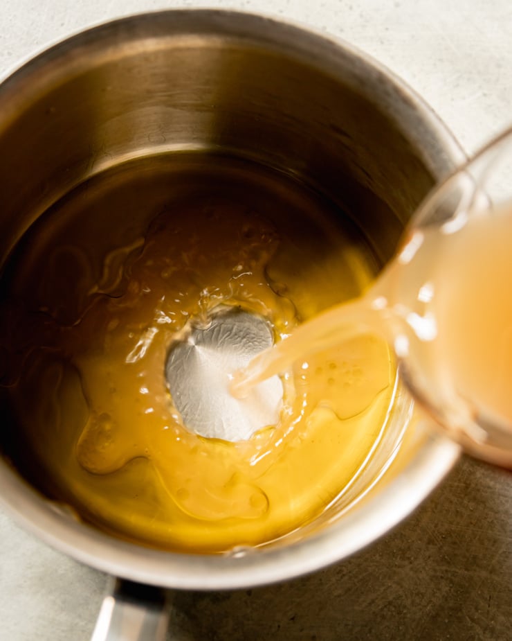 An overhead shot shows vegetable stock being added to olive oil in a pot.