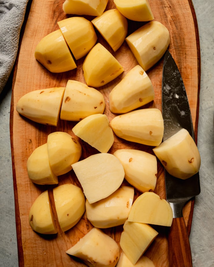 An overhead shot shows large dices of peeled potatoes on a wooden cutting board.