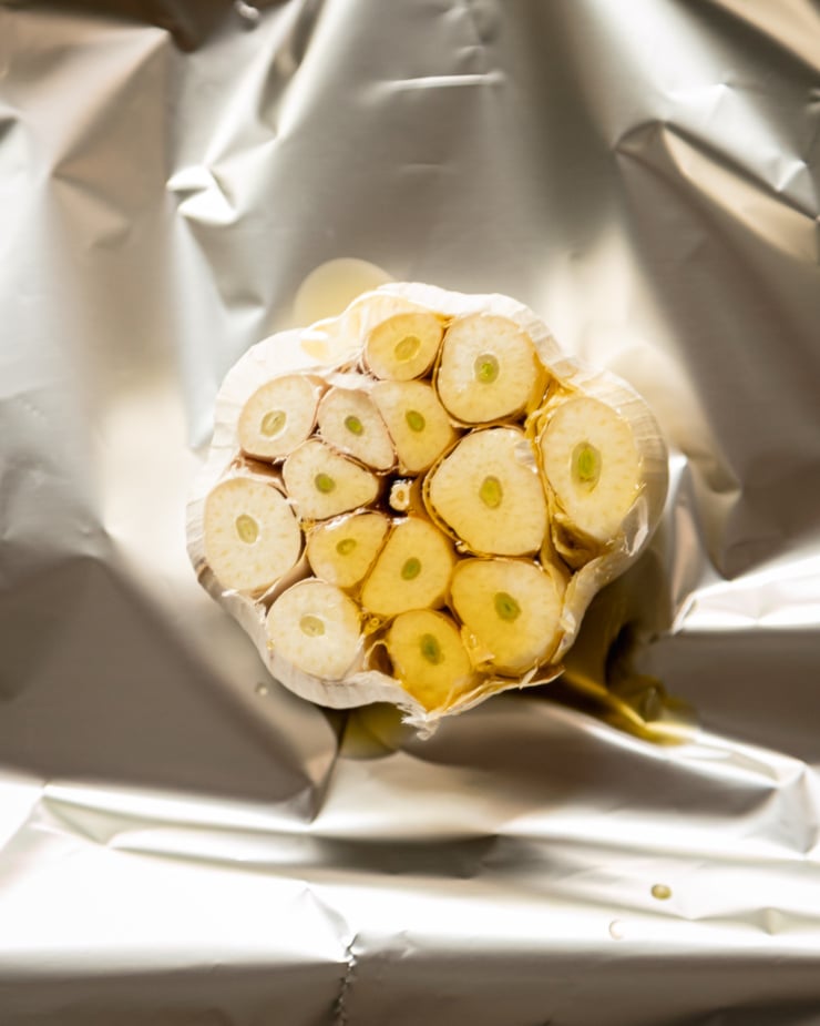 An overhead shot of a head of garlic with the top cut off, revealing the cloves inside. The garlic head is on top of aluminum foil.