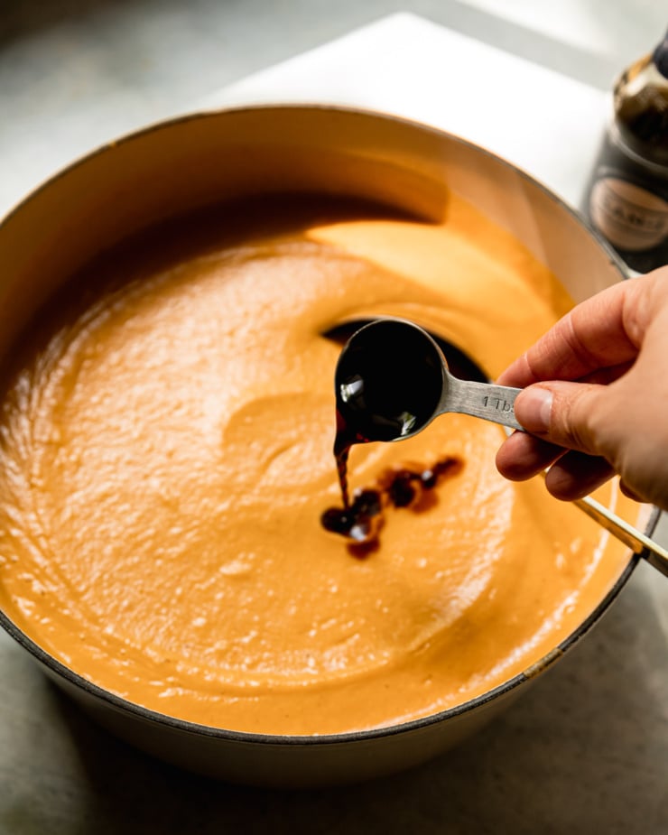 A 3/4 angle shot shows Tamari being added to a soup from a tablespoon measure.