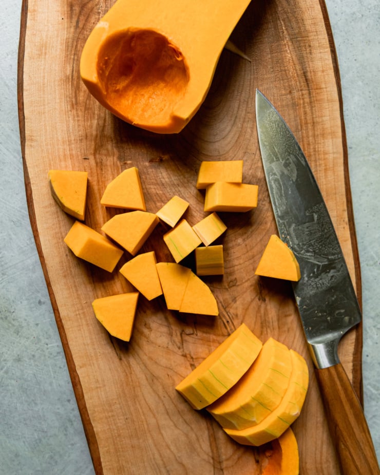 An overhead shot shows a peeled and seeded butternut squash that is in the process of being cut into slices and cubes.