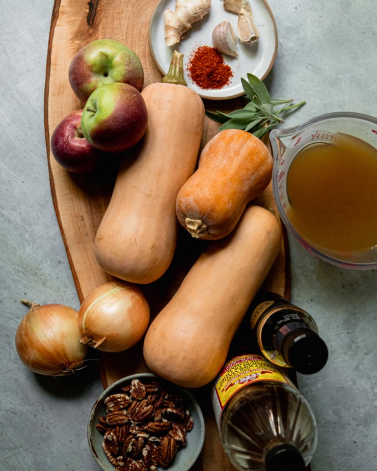 An overhead shot shows ingredients for a roasted vegan butternut squash soup with apples & pecans.