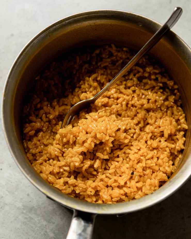 An overhead shot shows a small saucepan with golden garlic rice inside. A fork is in the pot.