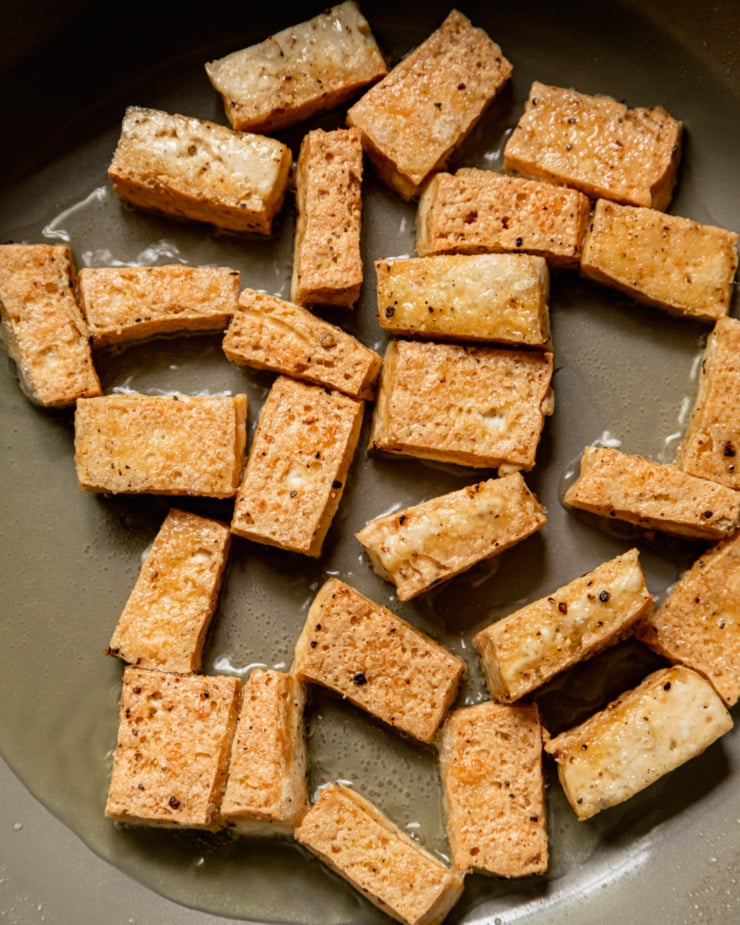An up close, overhead shot shows pieces of tofu frying in hot oil.