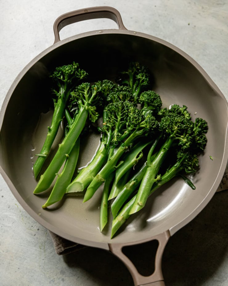 An overhead shot shows steamed broccolini stalks in a skillet.
