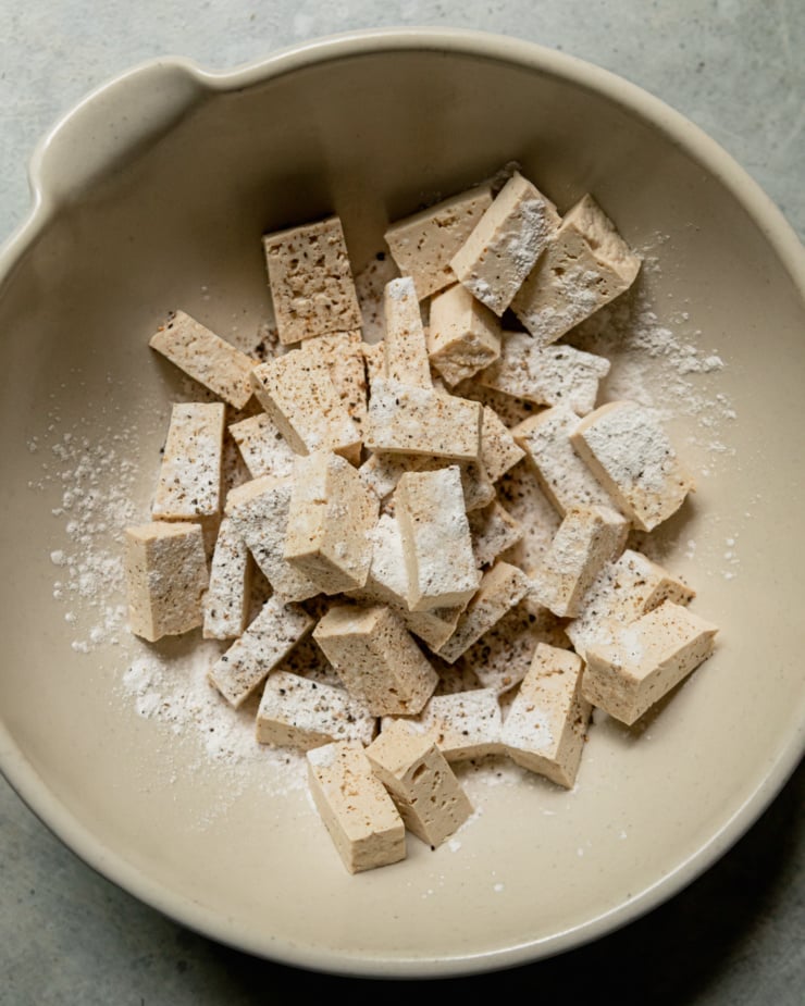 An overhead shot shows chopped tofu dusted with arrowroot starch, salt, and pepper.