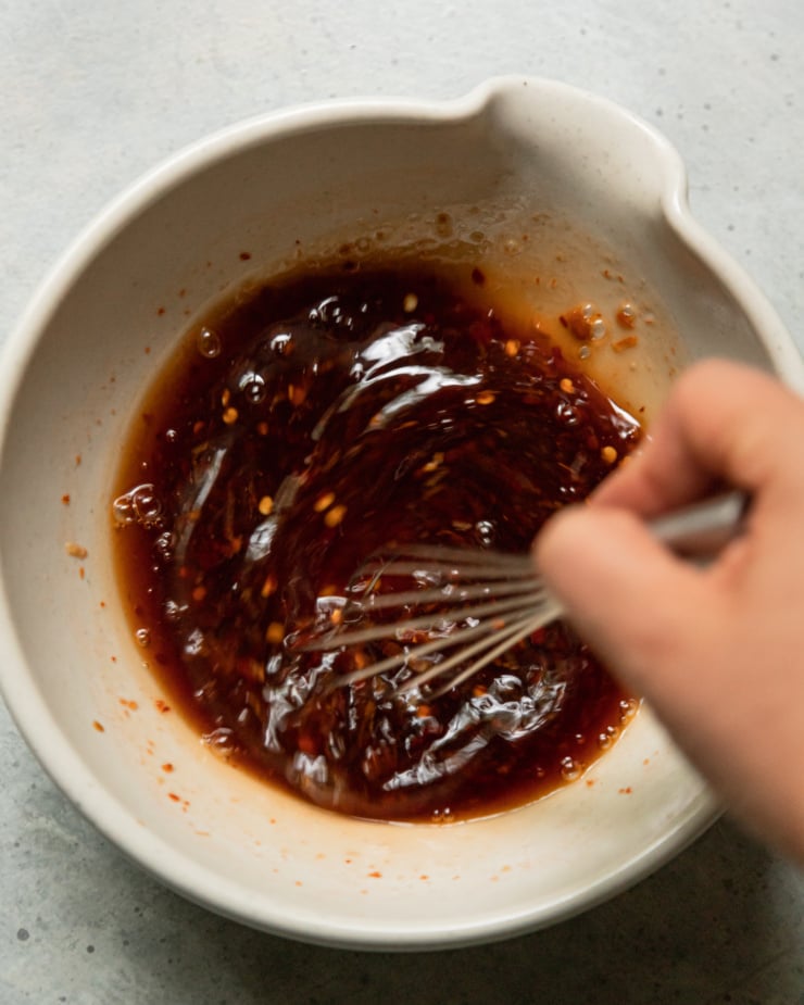 An overhead shot shows a hand using a whisk to bring a spicy maple sauce together in a bowl.