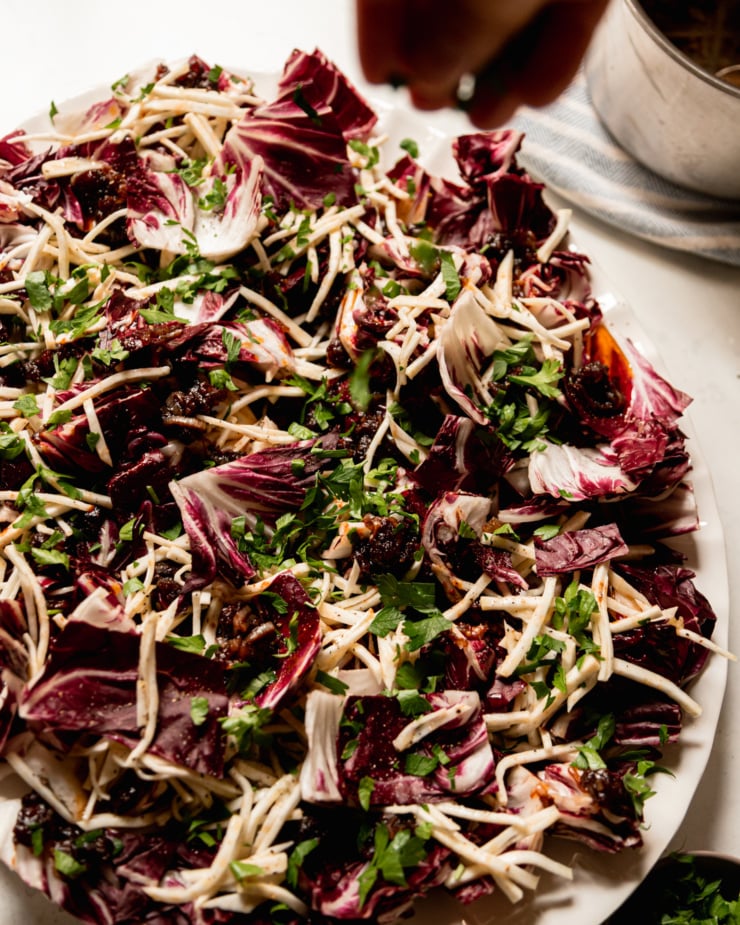 A 3/4 angle image shows a hand sprinkling parsley on top of a platter of radicchio and julienned celery root.