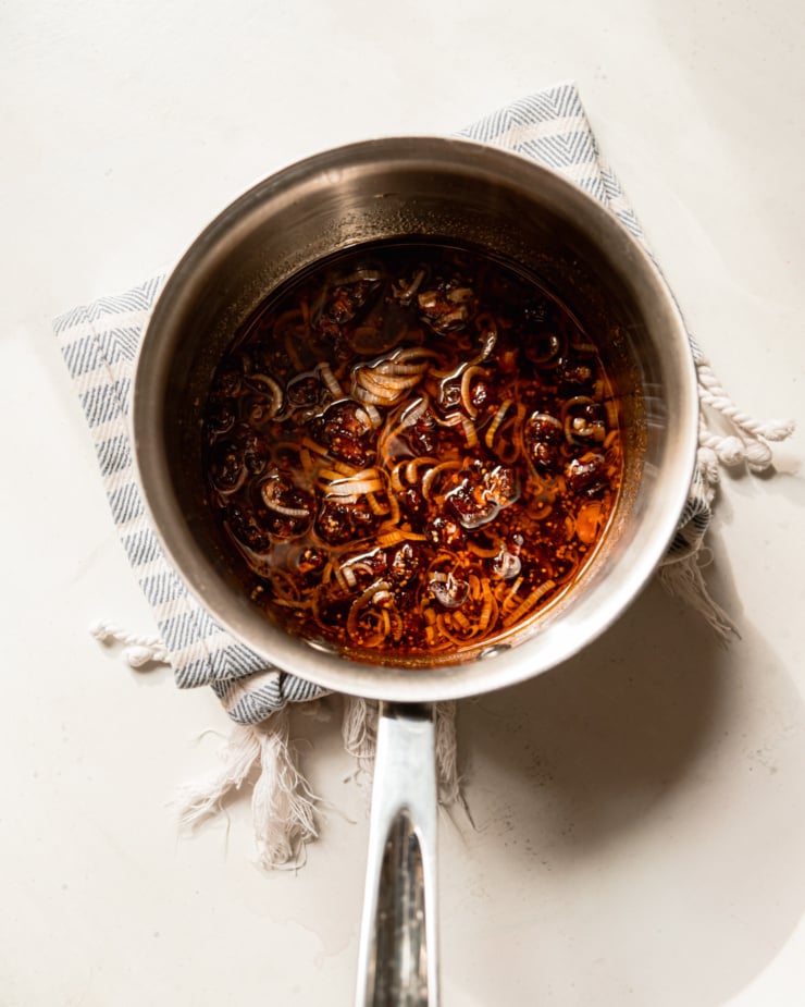 An overhead shot shows a saucepan with a warm date dressing, featuring shallots, smoked paprika, grainy mustard, olive oil, and balsamic vinegar.