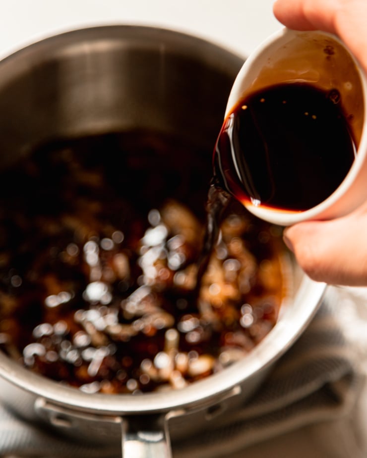 An overhead shot shows a hand pouring a bowl of balsamic vinegar into a saucepan.