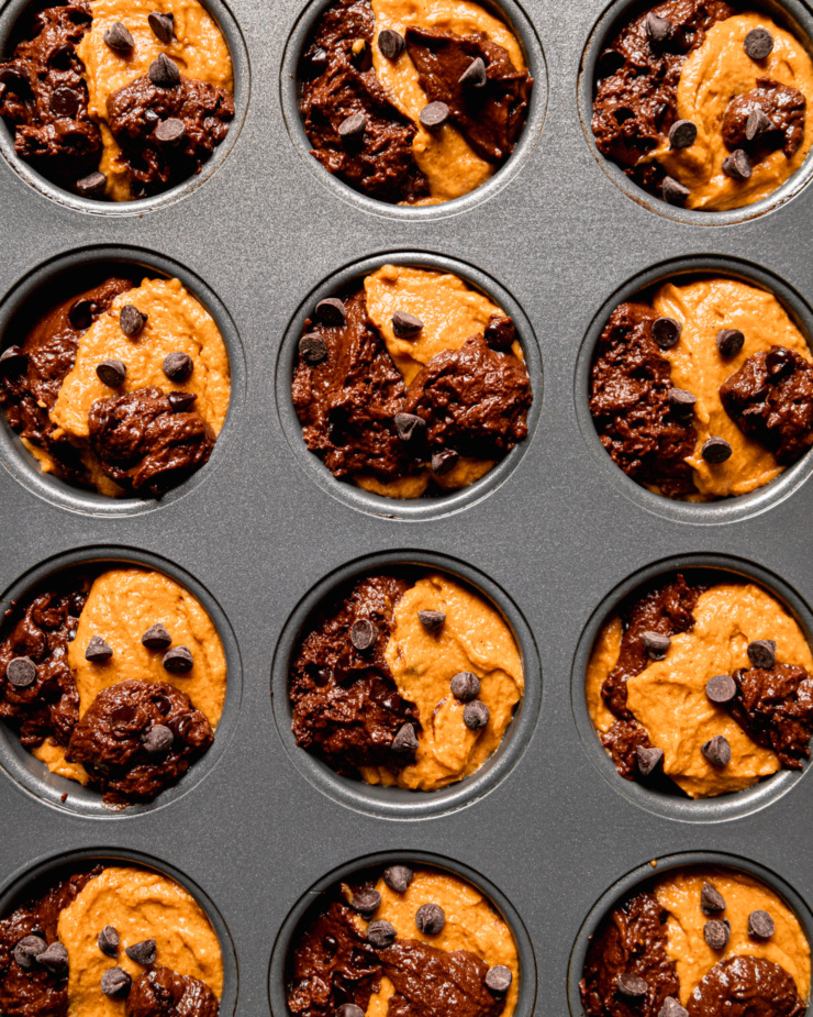 An overhead shot shows two batters portioned into a muffin tin. Each portion is topped with chocolate chips.