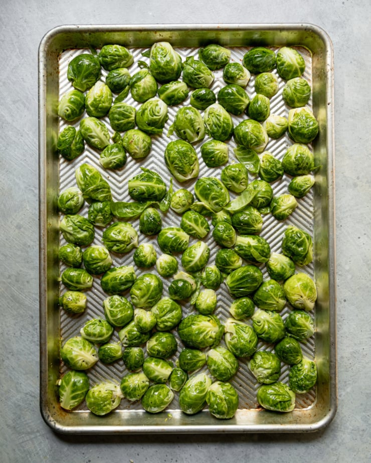 An overhead shot shows halved raw brussels sprouts coated in oil, salt, and, pepper, and all facing down on a baking sheet.