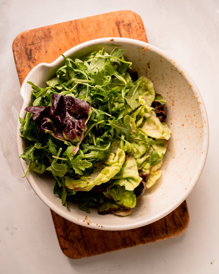 An overhead shot shows a bowl with torn bibb lettuce leaves and baby arugula.