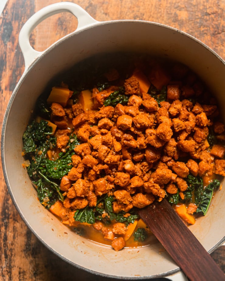 An overhead shot shows cooked pieces of vegan veggie sausage added on top of a soup.