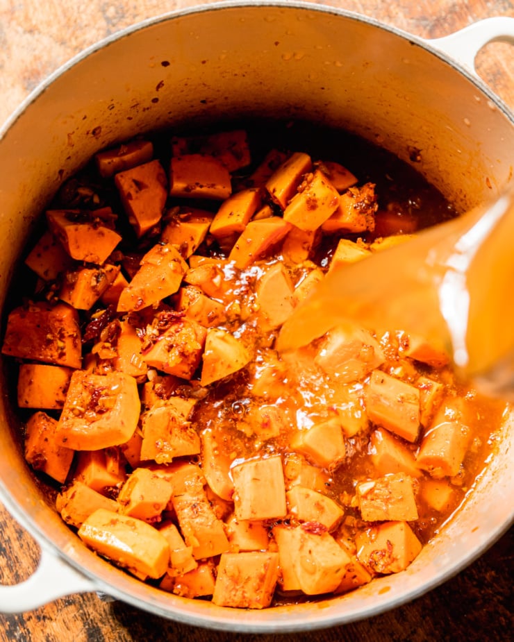 An overhead shot shows vegetable stock being poured into a pot with onions and butternut squash pieces.