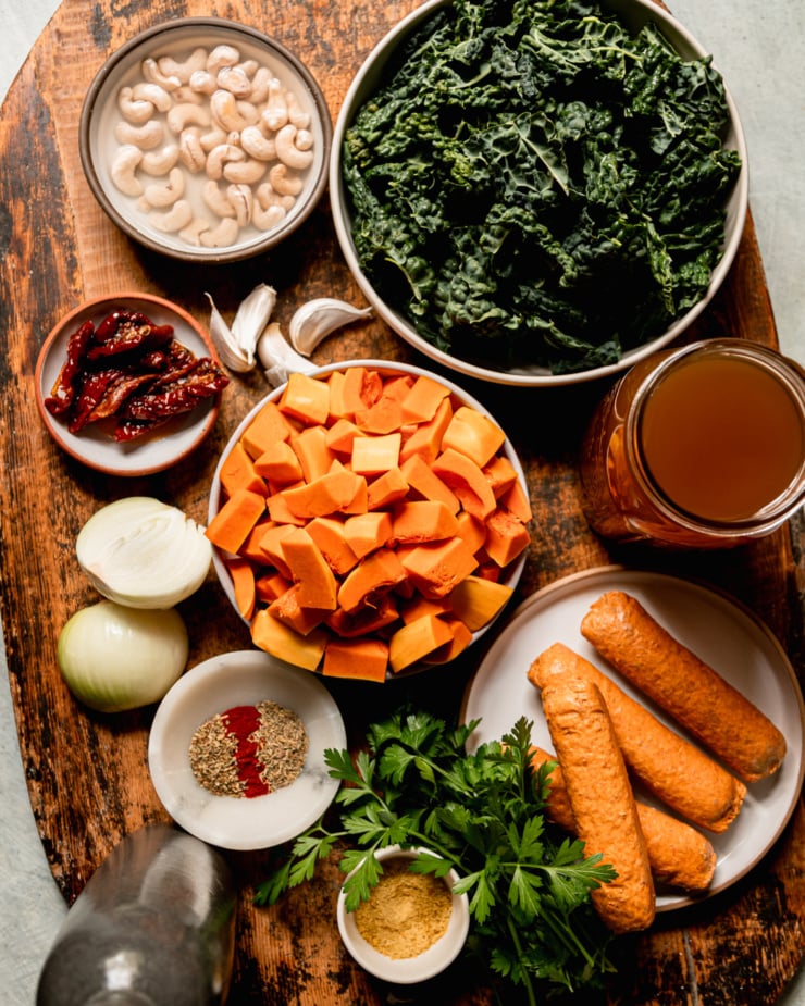 An overhead shot shows ingredients used in a vegan butternut squash zuppa Tosacana on a rough wooden board.
