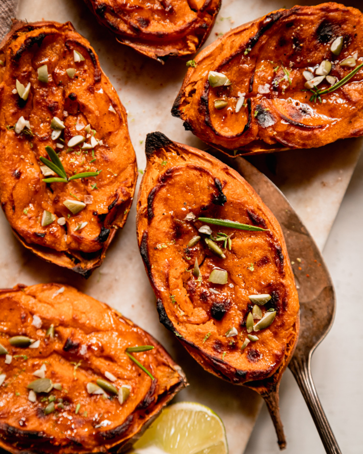 An overhead shot shows twice baked sweet potato halves garnished with thyme and rosemary leaves and chopped pumpkin seeds.