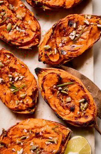 An overhead shot shows twice baked sweet potato halves garnished with thyme and rosemary leaves and chopped pumpkin seeds.