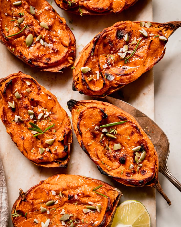 An overhead shot shows twice baked sweet potato halves garnished with thyme and rosemary leaves and chopped pumpkin seeds.