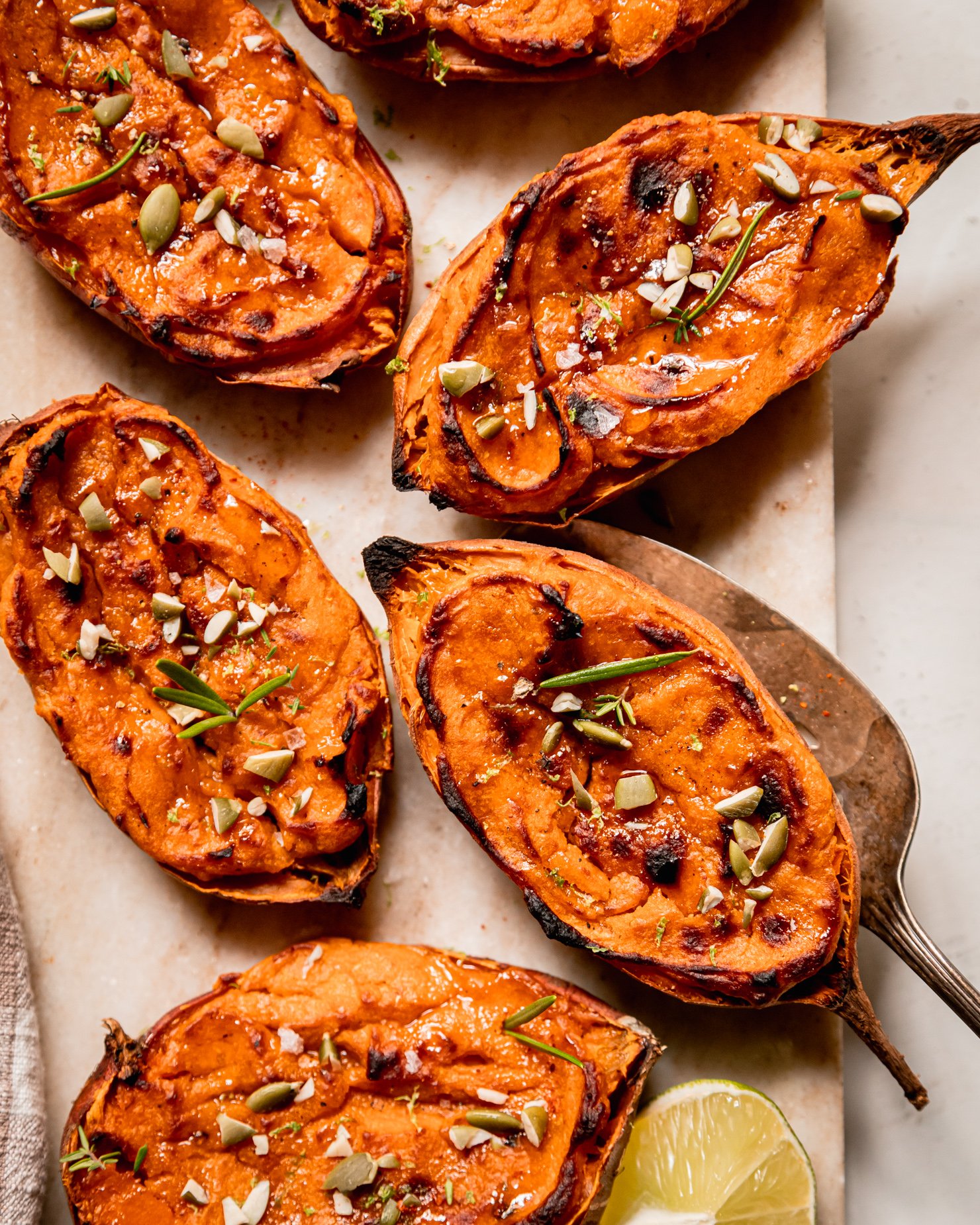 An overhead shot shows twice baked sweet potato halves garnished with thyme and rosemary leaves and chopped pumpkin seeds.