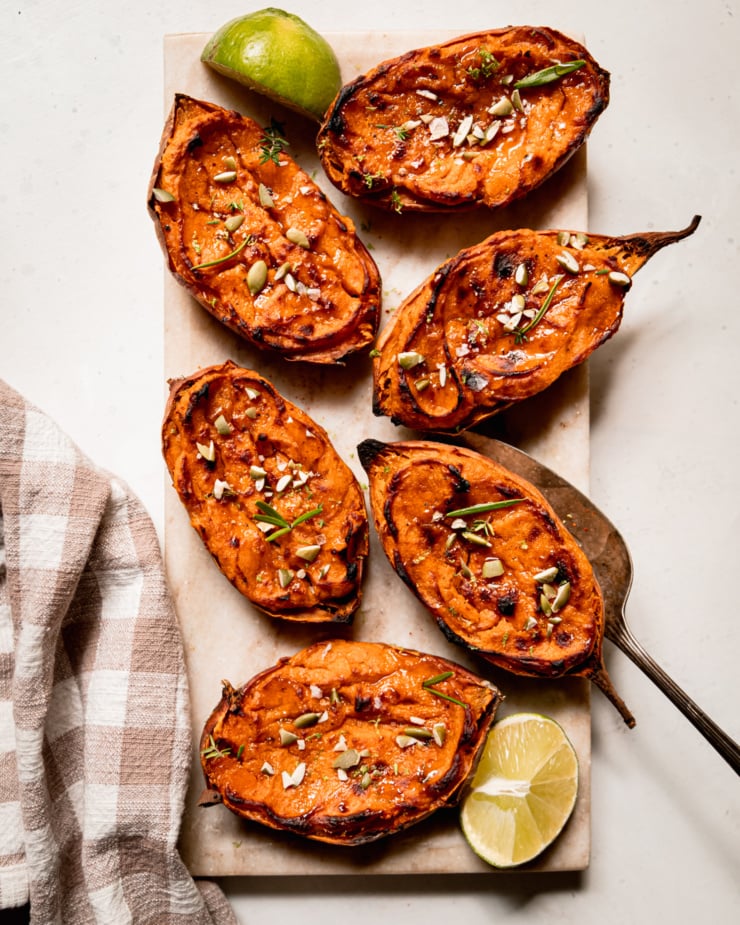An overhead shot shows twice baked sweet potato halves garnished with thyme and rosemary leaves and chopped pumpkin seeds.
