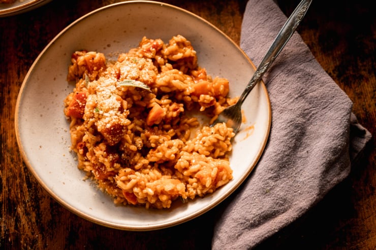 A 3/4 angle shot shows an individual serving of butternut squash risotto. A couple bites have been taken out of the serving.
