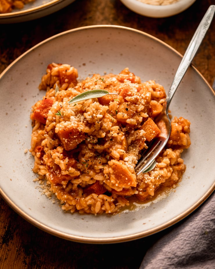 A slight 3/4 angle image shows a serving of vegan butternut squash risotto in a wide bowl. A fork is sticking out of the risotto.