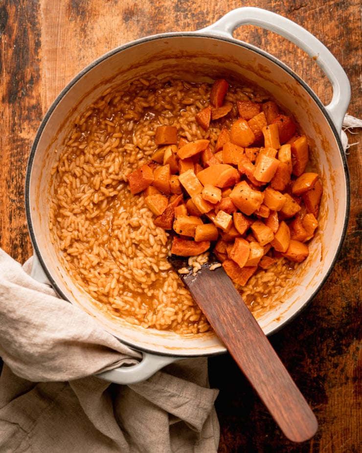 AN overhead shot shows roasted pieces of butternut squash on top of a vegan risotto in a Dutch oven-style pot.