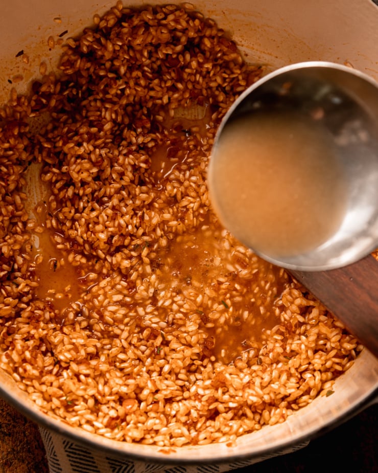An overhead shot shows a ladle of vegetable stock being added to a pot of arborio rice and seasonings.