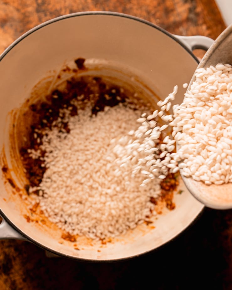 An overhead shot shows arborio rice being poured into a Dutch oven-style pot.