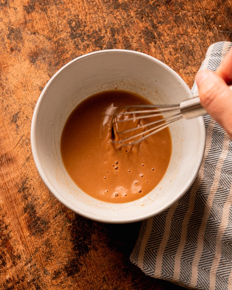 An overhead shot shows a hand using a whisk to stir miso into hot vegetable stock.