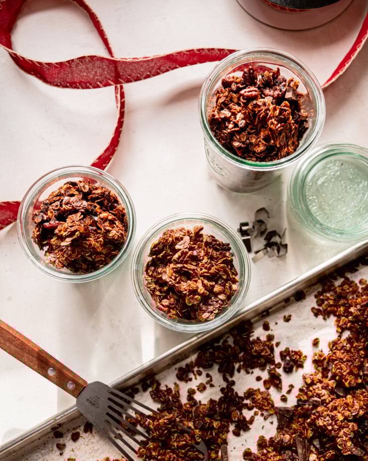 An overhead shot shows 3 jars of granola with some red ribbon nearby. The tray of granola is also in the frame.