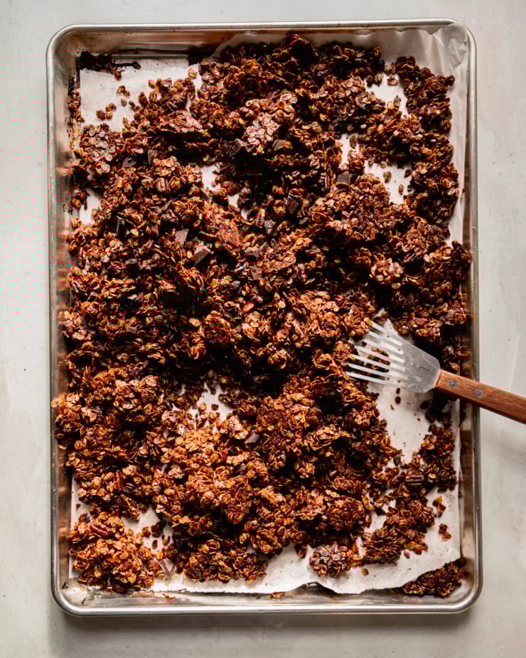 An overhead shot shows a baking sheet filled with ginger molasses granola. The granola is deep golden brown and features dark chocolate and dried cranberries.