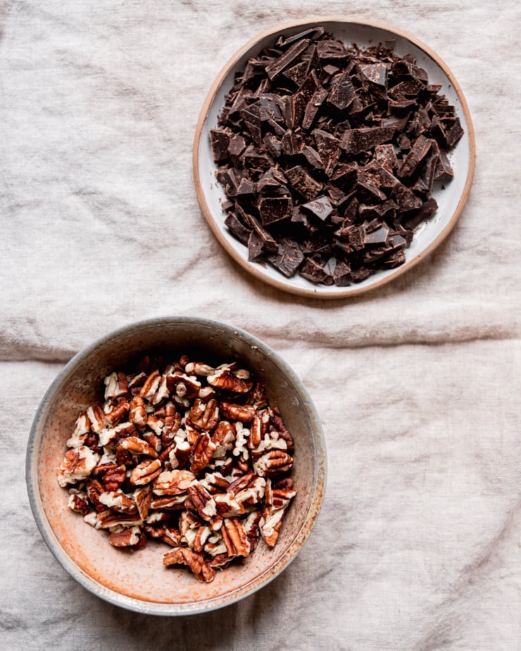 An overhead shot shows a bowl of chopped pecans and a small plate with chopped chocolate.