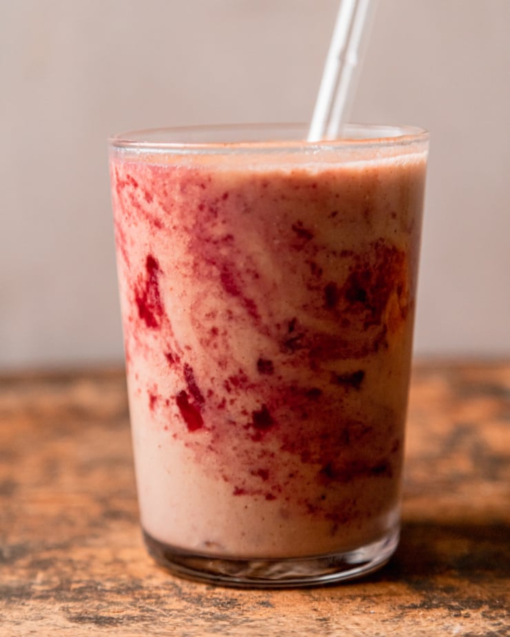 A head-on shot shows an orange cranberry smoothie in a glass with cranberry sauce/juice "tie dye" stripes on the side of the glass.
