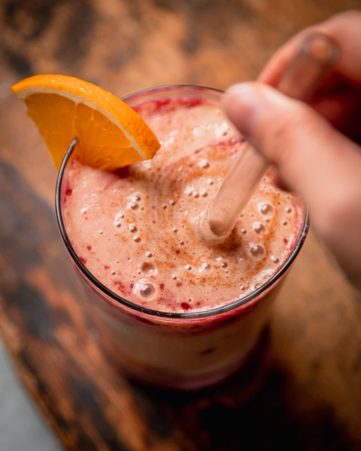 An overhead shot shows a hand using a straw to stir up a smoothie.