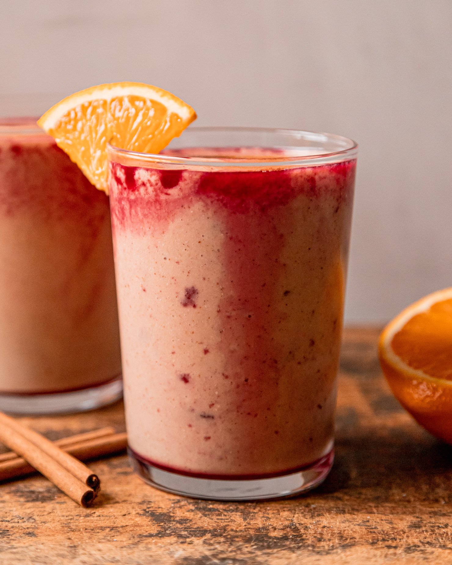 A head-on shot shows two glasses of orange cranberry smoothie, garnished with little orange slices on the rim.